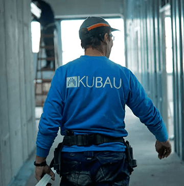 “Baustellen-Flur-mit-Kubau-MItarbeiter” Trockenbaumitarbeiter trägt Material durch einen Flur des Bauunternehmes